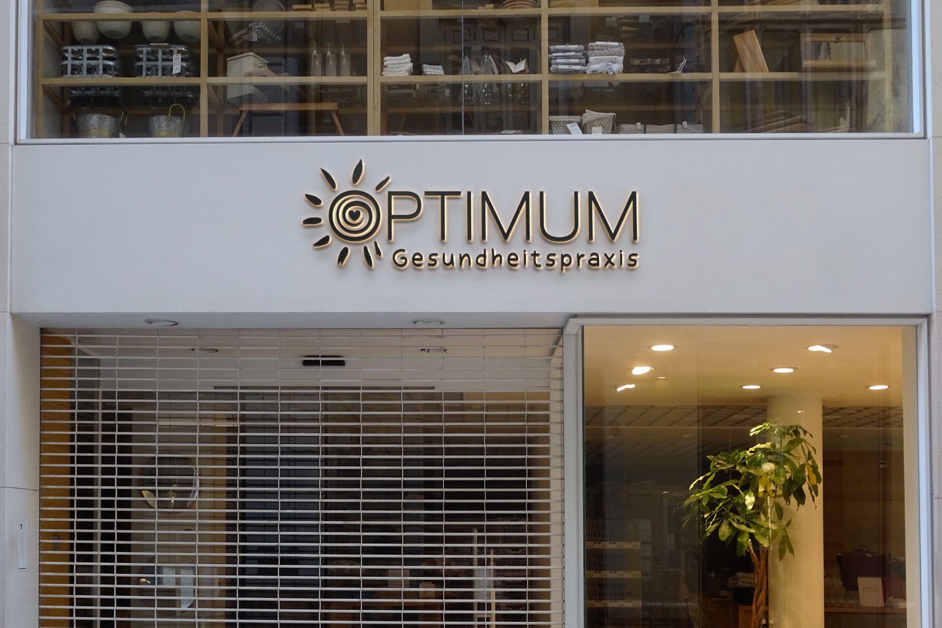 Leuchtendes Logo der Optimum Gesundheitspraxis an einer Fassade
